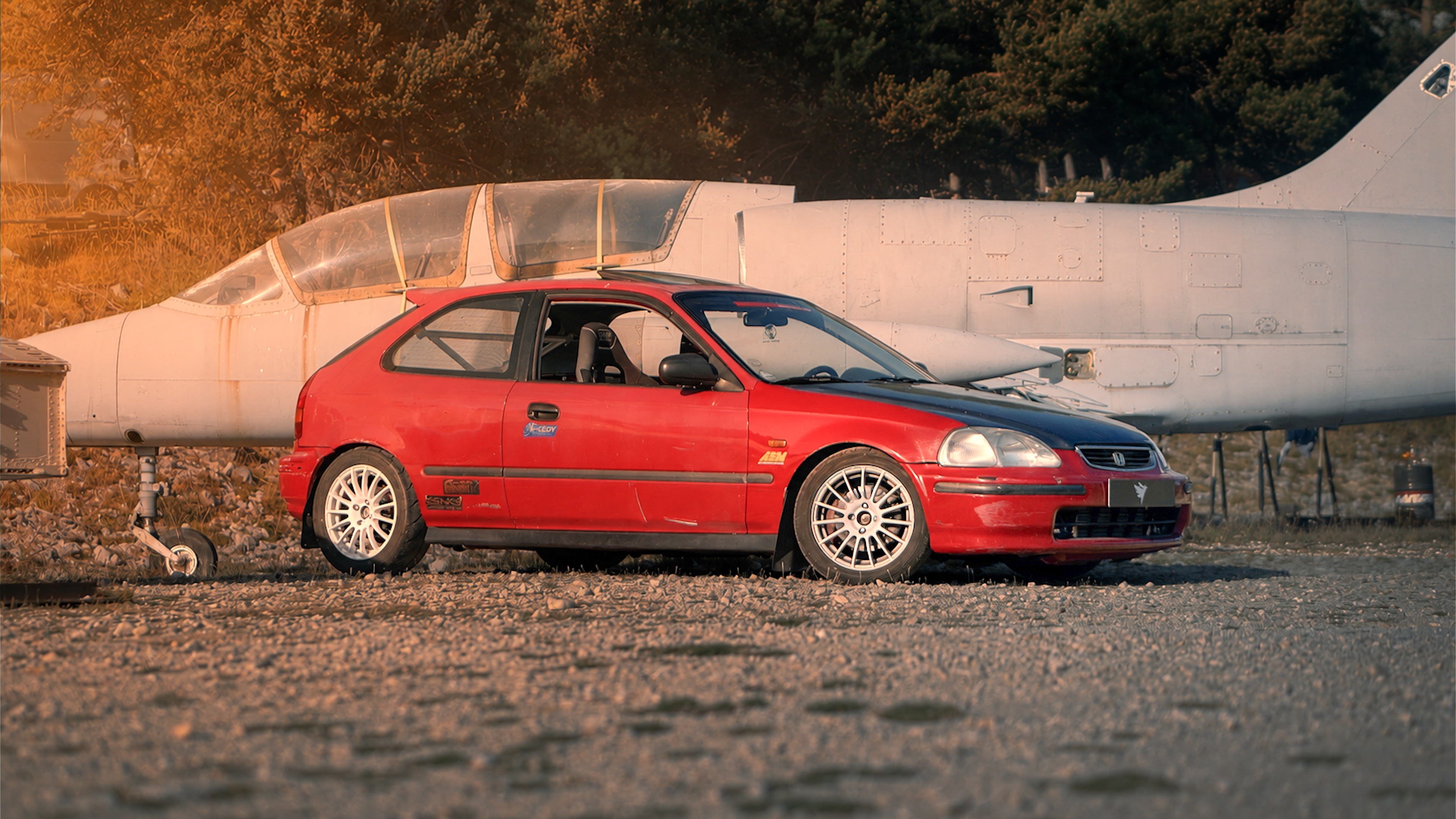 Honda rouge devant un avion au soleil couchant